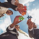 Outsourcing IT dla średnich firm – zespół układający wspólnie elementy układanki przed biurowcem