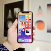 Służbowy iPhone w dłoni przy biurku z klawiaturą – aktualizacja iOS 27.2 w firmie