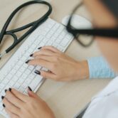 Wyciek danych NFZ eWUŚ – konto pracownika przychodni Pracownik przychodni przy klawiaturze i stetoskop – wyciek danych NFZ z systemu eWUŚ przez konta pracowników