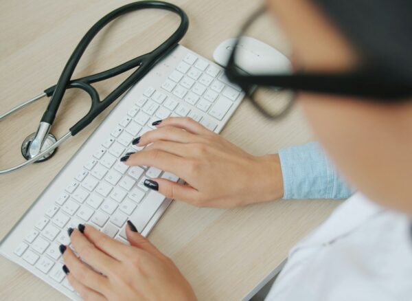 Wyciek danych NFZ eWUŚ – konto pracownika przychodni Pracownik przychodni przy klawiaturze i stetoskop – wyciek danych NFZ z systemu eWUŚ przez konta pracowników